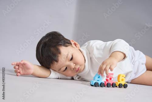 The child lies prone with arms stretched forward, near the toy cars.