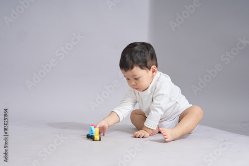 The child sits on knees, gently arranging or examining the toy cars lined up in front.