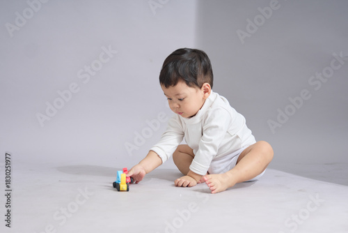The child kneels and carefully touches a row of small colorful toy cars with one hand.