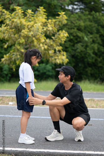 Asian father encouraging his daughter before a race, kneeling on the running track.