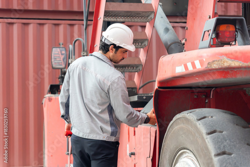 Industrial worker inspecting heavy machinery at container yard, Technician checking forklift equipment during cargo operations, Logistics worker performing safety inspection on heavy-duty vehicle