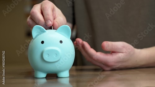 Watch as a person adds coins to a blue piggy bank at home. Each coin shows a step toward better savings and smarter money management in daily life. Make finances fun and easy.
