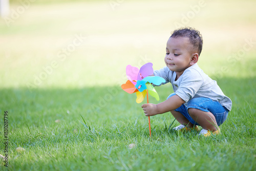 A boy enjoying a vibrant pinwheel in a park setting. He's surrounded by green grass and sunshine