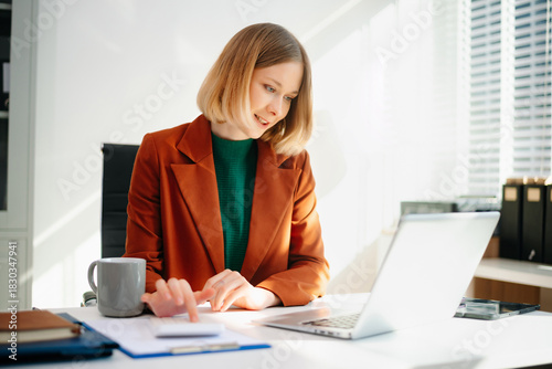 Business woman reviewing documents at desk in modern office. Ideal for finance, marketing, startup workflow, data analysis, productivity, and remote work themes.