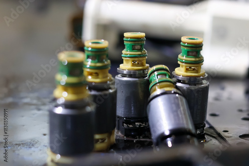 Tableau sur toile ​A cluster of automatic transmission solenoid valves standing on a wet surface, featuring metallic bodies and distinct yellow and green electrical connectors, signifying diagnostic