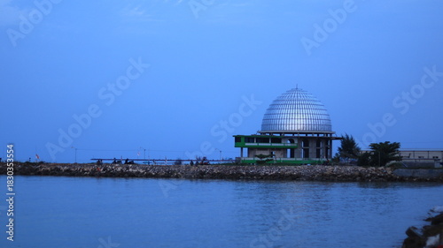 A green mosque with a large silver dome is located on the beach in the northern coastal tourist area of ​​Tuban, Indonesia.