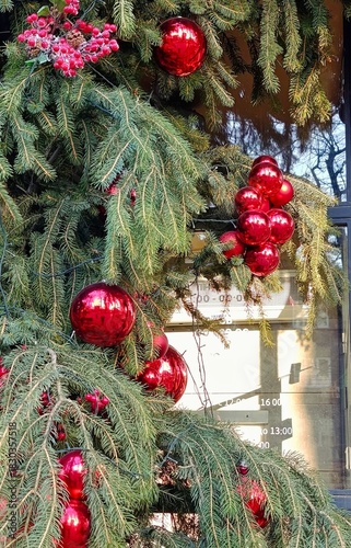 Close-up of Christmas decorations made of fir branches and shiny red ornaments with reflections. Festive holiday composition featuring traditional winter decor and bright seasonal colors.