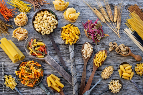 Different types of uncooked pasta on rustic wooden table, in the spoons, cutting board and bowls 