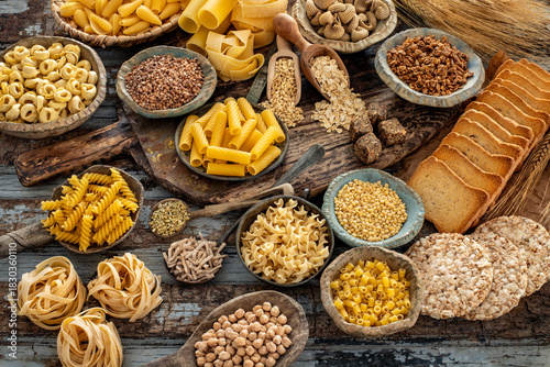 Different types of uncooked pasta on rustic wooden table, in the spoons, cutting board and bowls 