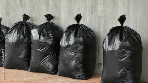 Dumps of black trash bags stacked along a concrete wall in an urban area during daylight hours