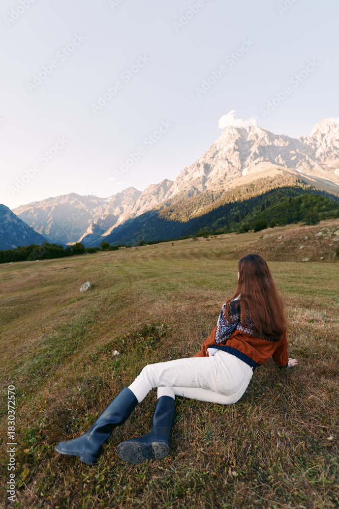 Naklejka premium Woman lying on grass in a mountain meadow, boots visible, peaceful landscape and nature scene for outdoor relaxation, travel and scenic summit view at golden hour.