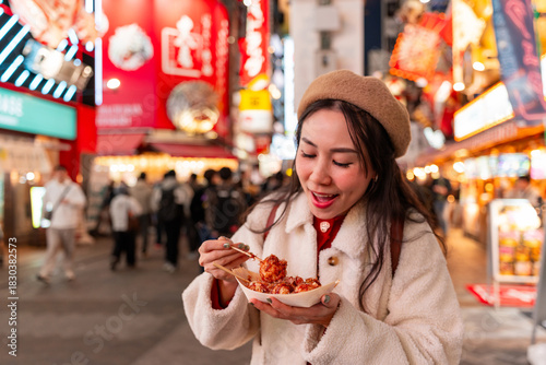 Bild auf Leinwand Young female tourist enjoys eating takoyaki the traditional popular food in Doto