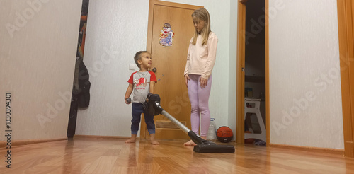 Young boy talking while standing next to sister vacuuming indoors  