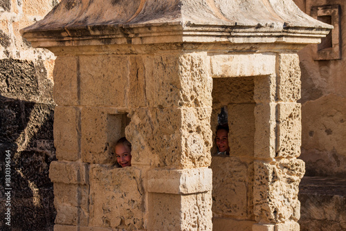Bild auf Leinwand Two smiling sisters framed by a watch tower window in an ancient castle construction during a sunny spring day