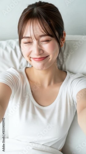 寝室のベッドで優しく微笑みながら自撮りをする若い女性