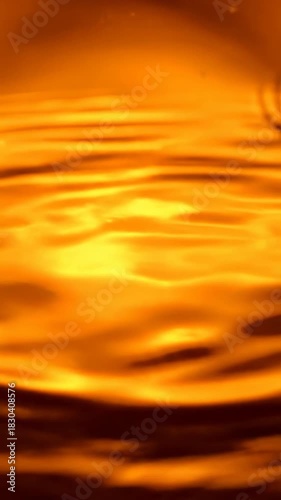 Gentle slow motion abstract liquid ripple effect expanding in warm golden orange colors across a smooth surface luxury, slow, fluid