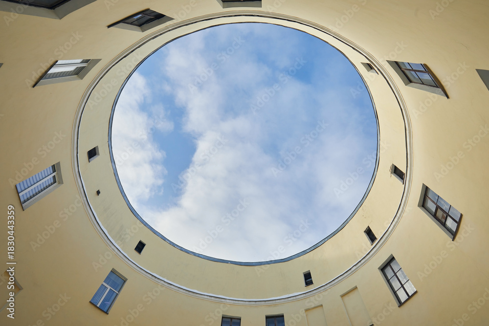 Fototapeta premium A round courtyard of a house with a view upwards to a blue sky with clouds