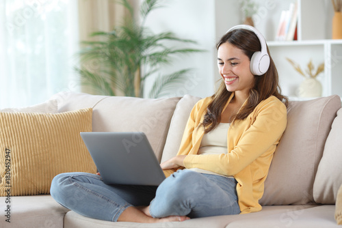 Happy woman in yellow wearing headphone watching media on laptop