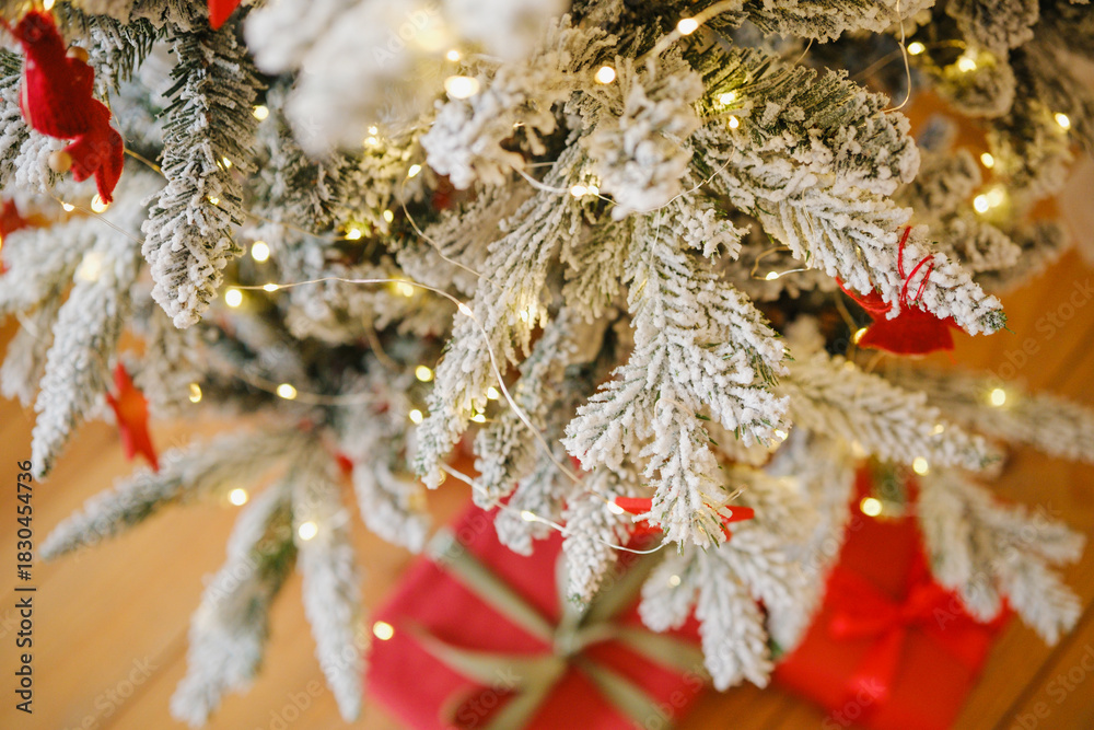 Obraz premium Snowy evergreen branches with glowing warm lights and red wrapped gifts below