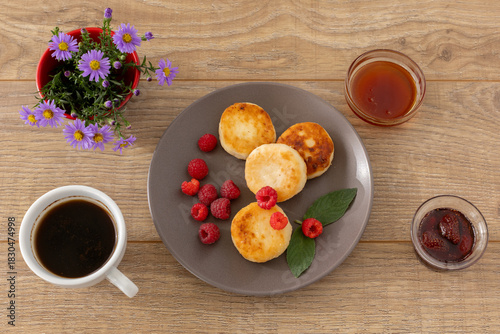 Foto Cup of coffee and curd fritters with raspberries on the wooden background