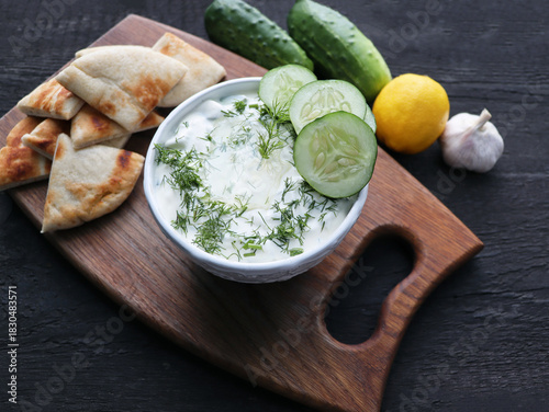 Tzatziki sauce with ingredients cucumber, garlic dill, lemon on darky background. Healthy food