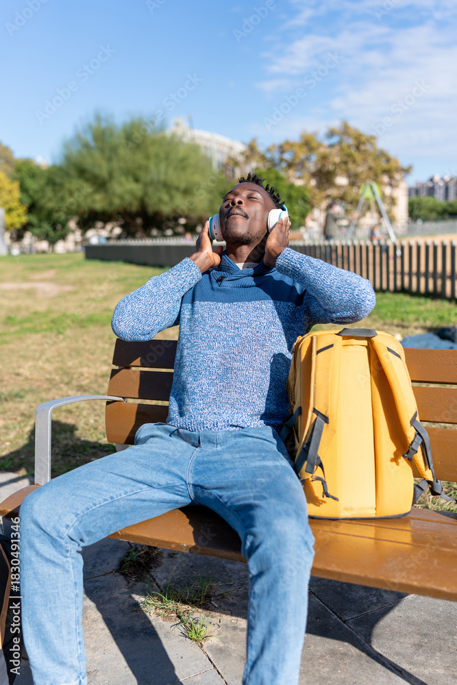 Fototapeta premium African American man relaxing on park bench listening to music with headphones
