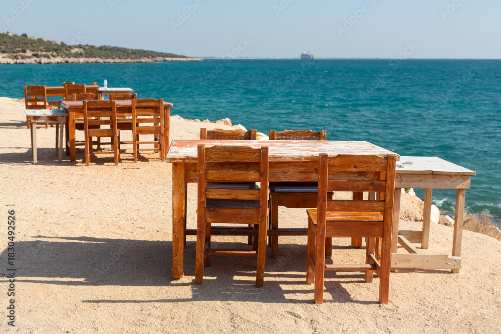 Fototapeta premium Wooden table and chairs on a beach by the Mediterranean Sea.