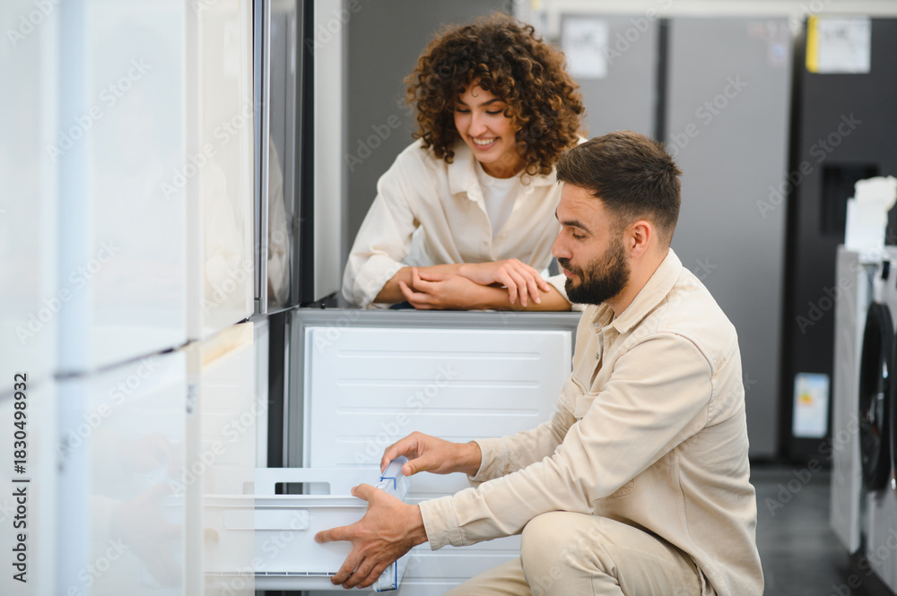 Fototapeta premium Couple choosing refrigerator in electronics store, examining features together