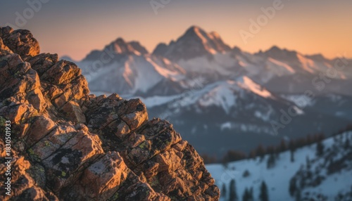 Sunset light warms rugged mountain rocks above snowy alpine valley in winter