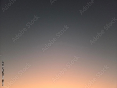 Minimalist gradient sky background showing a transition from a dark, muted grey/blue at the top to a soft, light orange/peach color at the bottom, suggesting twilight or sunset.