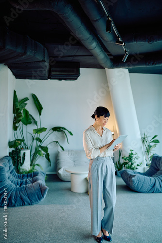 Businesswoman standing, working with a tablet in a contemporary office lounge, combining professional technology with a green interior