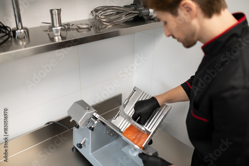 Man in uniform slicing meat with professional slicer