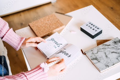 Person sits at desk writing goals for year in notebook next to light box displaying FRESH START. New Year resolutions, goal setting, planning, personal development.