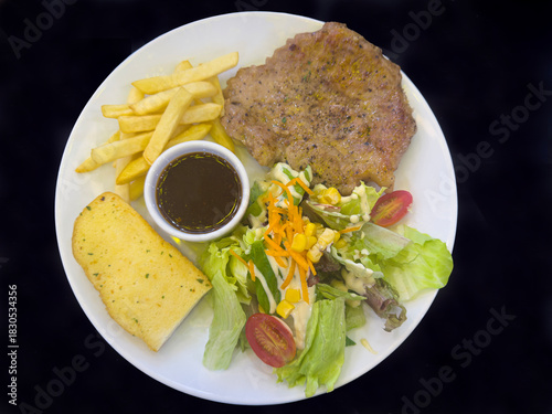 Thinly sliced ​​pork steak served with salad, garlic bread and french fries on a white plate.