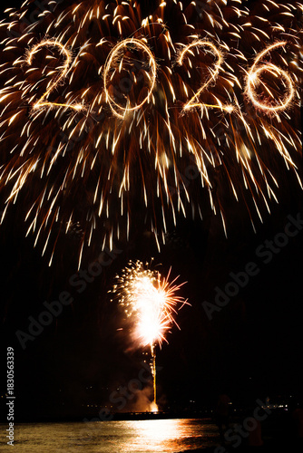 2026 happy new year text of sparklers and colorful fireworks in the night sky over sea surface