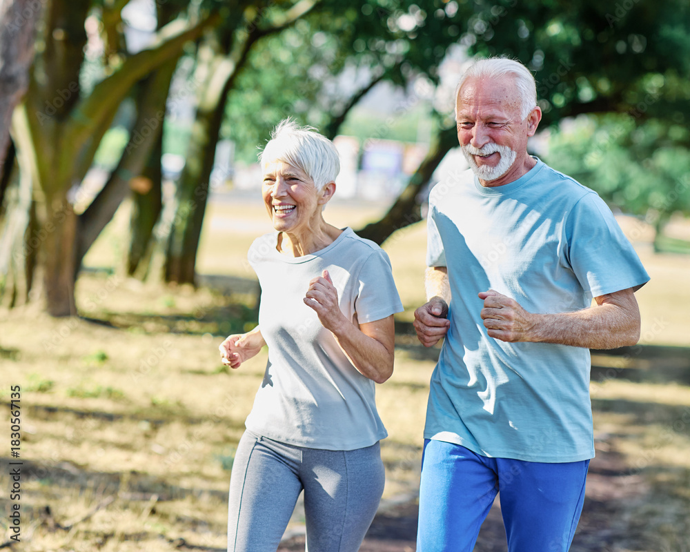 Fototapeta premium Smiling active mature senior couple jogging together in the park
