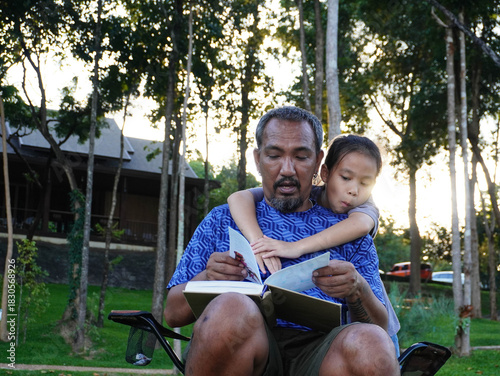 Father and Daughter Reading Book Together Outdoors in the Sunset Light.