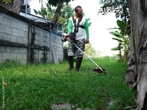 Man Using Brush Cutter to Mow Tall Grass for Yard Maintenance and Gardening.