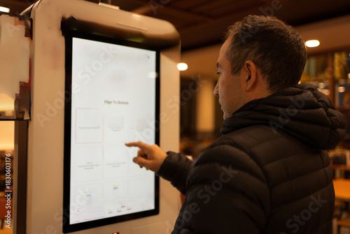 Obraz na plátně Man using touchscreen self-service kiosk ordering food or drinks