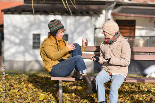 Mother and young adult daughter talking on a park bench in autumn