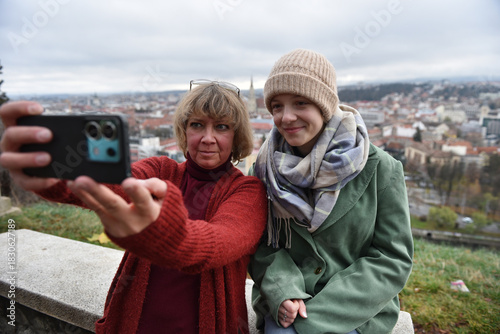 Mother and young adult teenager daughter taking a selfie outdoors with a city view