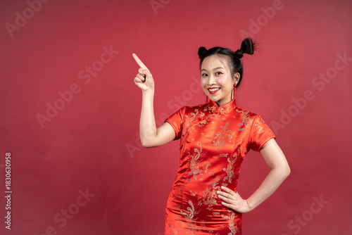 Happy Asian woman in Cheongsam pointing finger at copy space on red background.