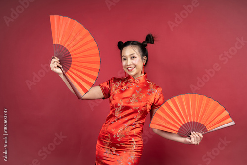 Happy Chinese girl in Cheongsam holding traditional paper fans in studio