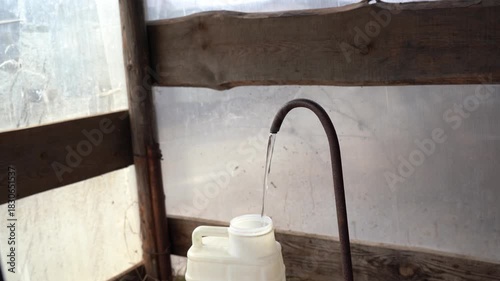 A person stands beside a water source, filling a container with water, showcasing the simple act of gathering fresh water in a rustic environment.. Video with sound