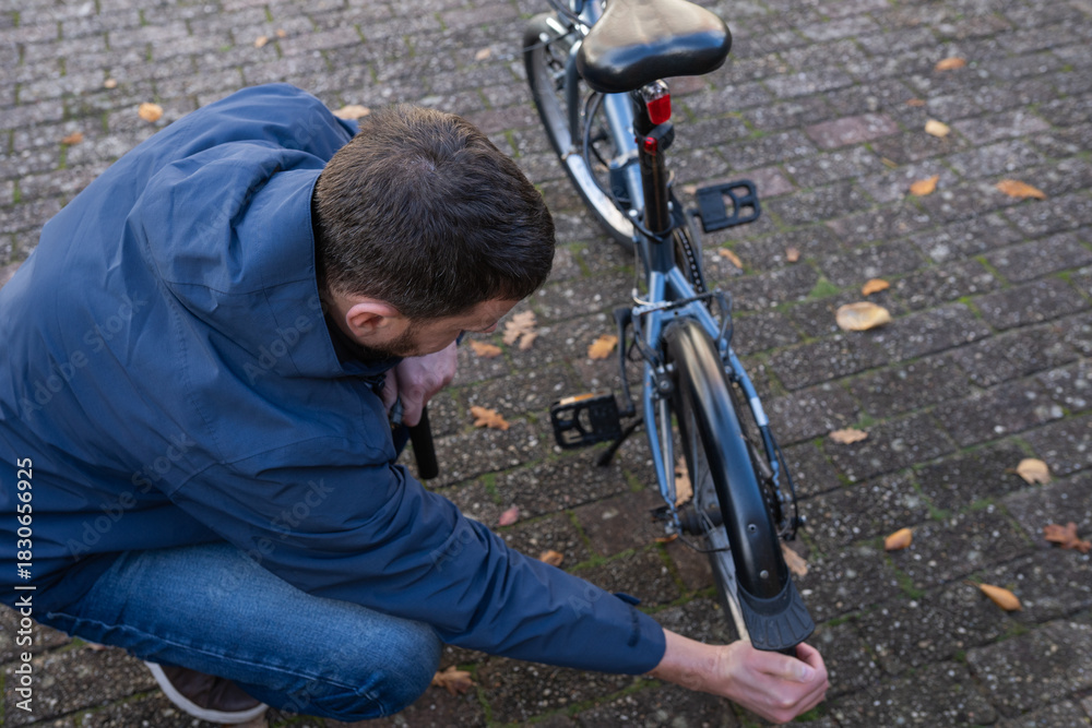 Obraz premium A man carefully inflates the tire of a folding bicycle with a portable pump, ensuring optimal pressure for his upcoming ride. Moment highlights preparation and self-reliance in urban cycling.
