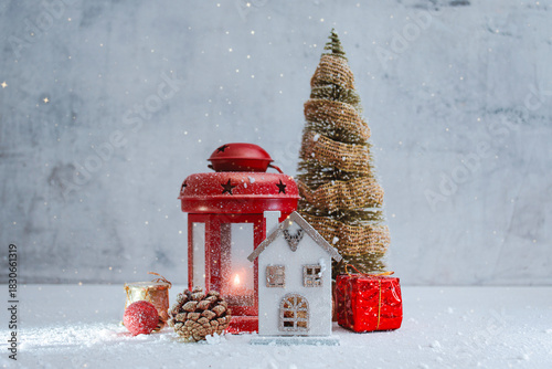 Festive Christmas scene with red lantern with a glowing light, miniature house, gifts and a decorative Christmas tree with snow. Winter composition for seasonal greeting cards and New Year.