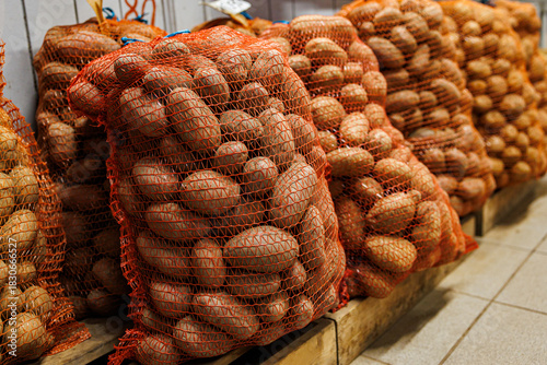 Large sacks of potatoes stored in red mesh bags, stacked on wooden pallets indoors at a wholesale or market facility