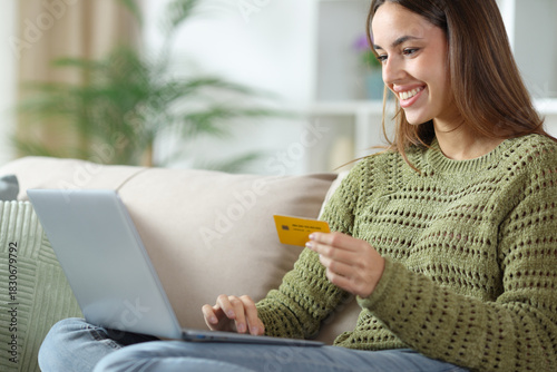 Happy woman in green paying online with laptop and card