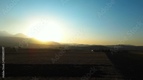 A dramatic sunset scene captured by a drone, featuring silhouettes of crows gliding across the colorful sky as warm evening light spreads over the landscape.