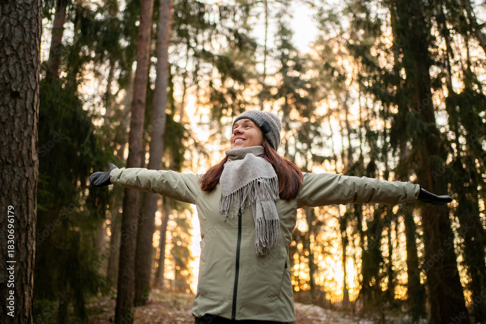 Naklejka premium Woman in forest in winter. Happy in nature in Finland. Trees in woods. Healthy Finnish outdoor lifestyle. Smiling person arms raised. Fresh air.